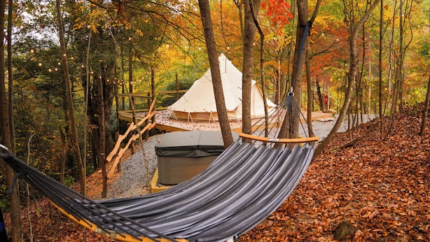 A hammock in a forest with a tent and a small outdoor seating area. - Glamping! Campsite #5 (Waynesville)