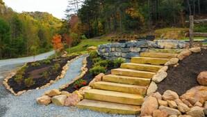 A stone staircase leading up a hill, surrounded by a garden with red flowers and a forest in the background. - Glamping! Campsite #5 (Waynesville)