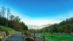 A gravel path with a wooden fence, a stone wall, and a grassy area with trees and a clear sky. - Glamping! Campsite #5 (Waynesville)