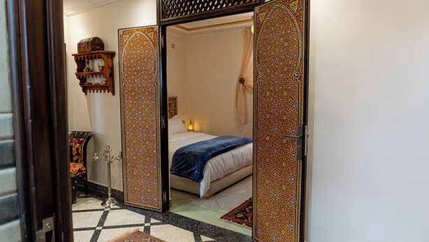 Una habitación con cama, mesita de noche, lámpara y un espejo decorativo.
