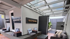 A covered outdoor seating area with wooden flooring and modern furniture. - Entire Private Lodge for Exclusive Use-Perfect for Groups (Normanville)