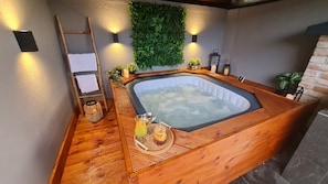 Spa-område med jacuzzi, trægulv, en stige, vægmonterede lamper og en grøn væg.