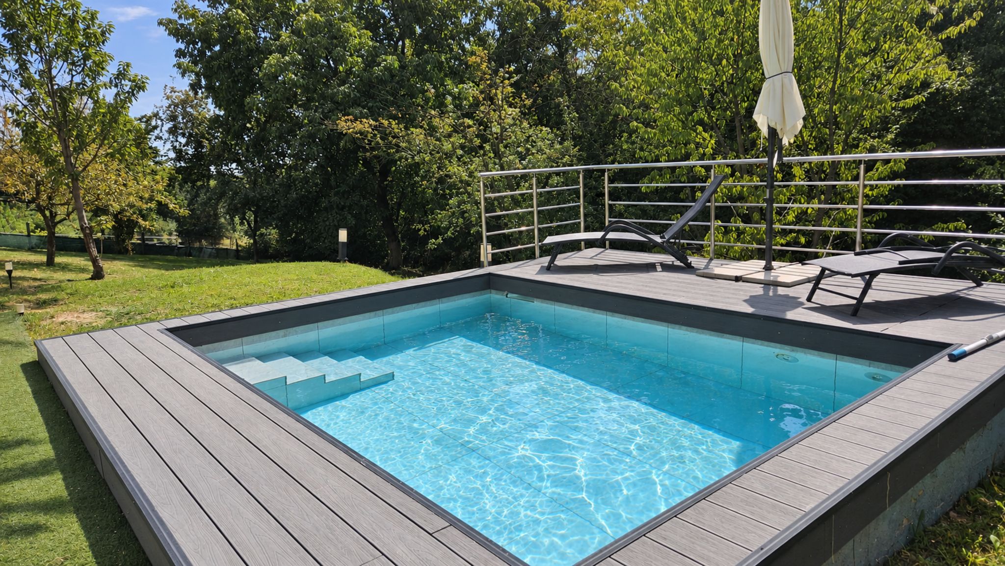 A rectangular swimming pool with a wooden deck and metal railing.