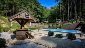 Une cabane en bois avec une piscine, entourée d’une zone boisée et d’une aire de jeux.