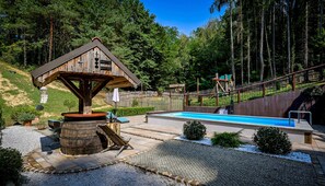 Eine Holzhütte mit Pool, umgeben von Wald und einem Spielplatz.