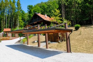 A wooden house with a red roof, a wooden staircase, and a gravel driveway.