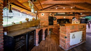 Une cuisine rustique avec un four en briques, des poutres en bois et une grande fenêtre donnant sur une clôture blanche.