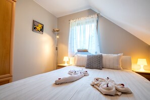 Een hotelkamer met een netjes opgemaakt bed, een bedlampje, een raam met dunne gordijnen en een schilderij aan de muur.