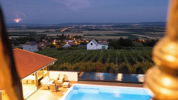 A pool area with a view of vineyards and distant city lights. - Luxury villa with jacuzzi, sauna and pool surrounded by vineyards (Požega)