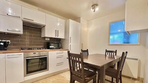 A modern kitchen with white cabinets, a built-in oven, a microwave, and a dining table with four chairs. - Right Opposite Whitechapel Station (London)