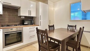 A modern kitchen with white cabinets, a built-in oven, and a dining table with four chairs. - Right Opposite Whitechapel Station (London)