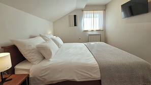Ein Schlafzimmer mit einem Bett, Kissen, einem Nachttisch mit Lampe, einer Heizung und einem an der Wand befestigten Fernseher.