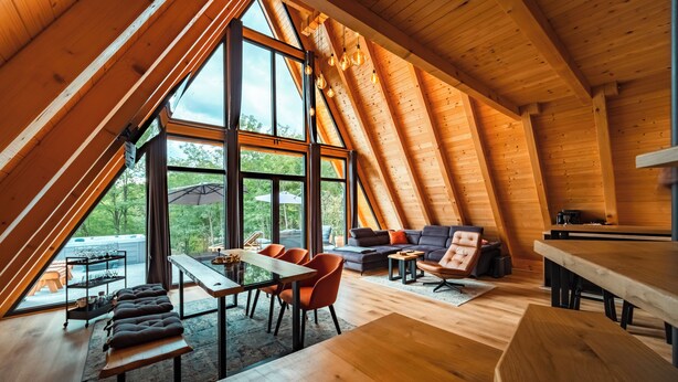 Ein gemütliches Holzinnenleben mit hohen Decken, einem Essbereich, einer Couch und großen Fenstern mit Blick ins Freie.