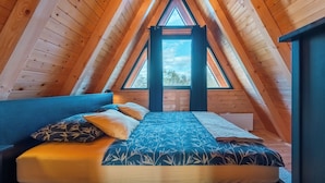 Ein gemütliches Schlafzimmer im Dachgeschoss mit holzgetäfelter Schräge, einem großen Fenster und einem Bett mit gemusterten Betttextilien.
