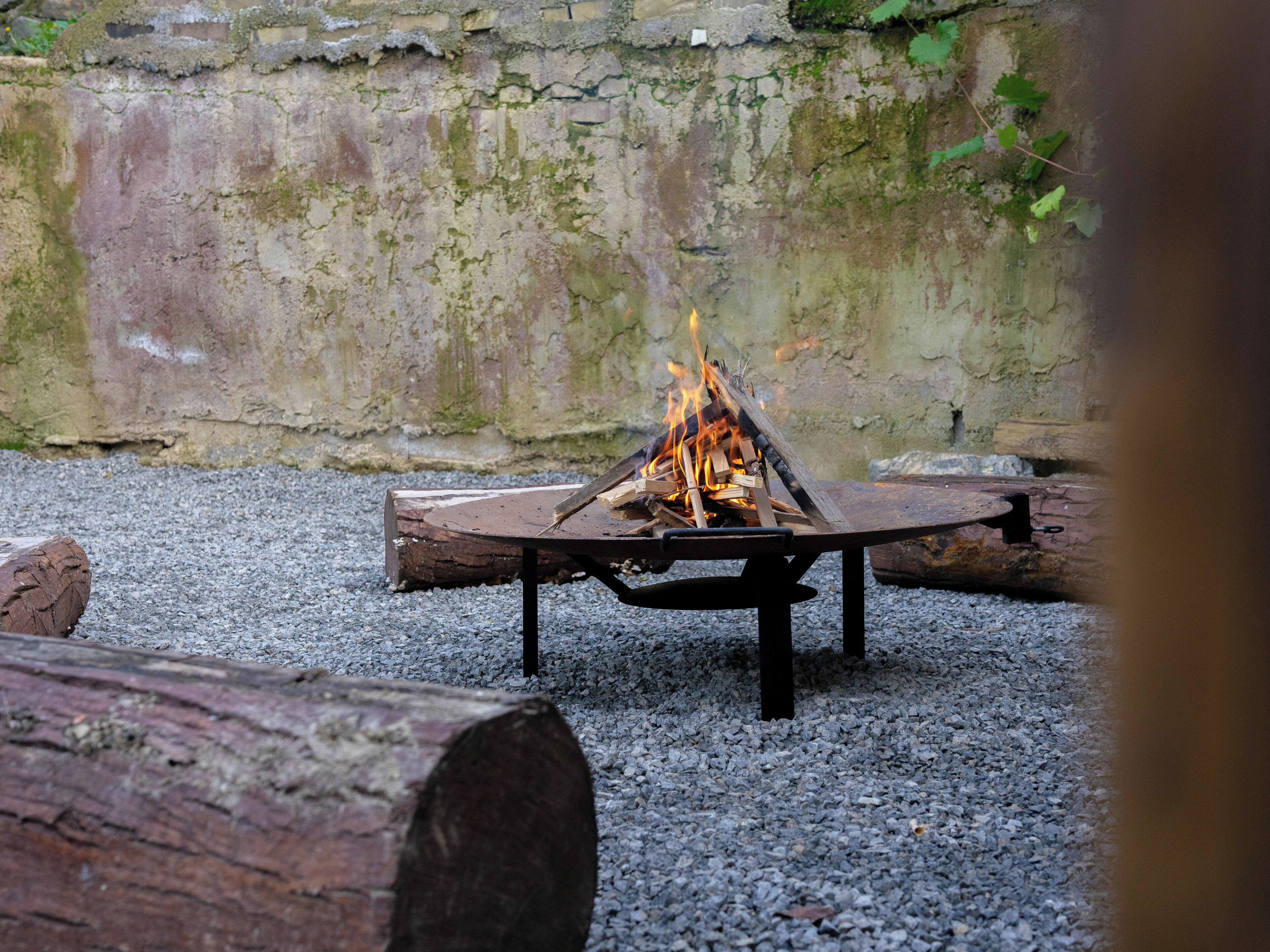 Un feu de camp avec des bûches et du petit bois, entouré de gravier et d’un muret en pierre.