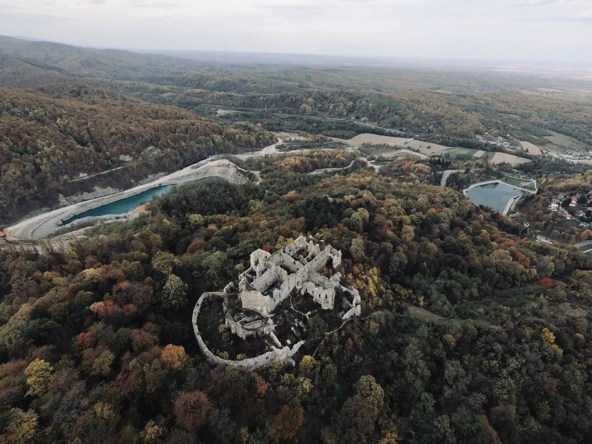 Vista aèria d'un castell històric envoltat de bosc dens i un riu.