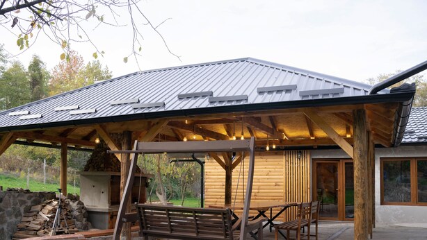 Un espace extérieur abrité avec des balançoires, des bancs en bois et une cheminée en pierre.