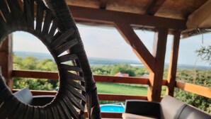 Een overdekt terras met uitzicht op een groen landschap en een zwembad.