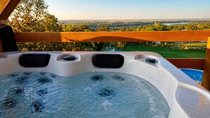 Een hottub met een houten terras en een prachtig uitzicht op een meer en bos.