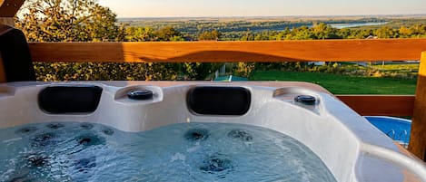 A hot tub with a wooden deck and a scenic view of a lake and forest.