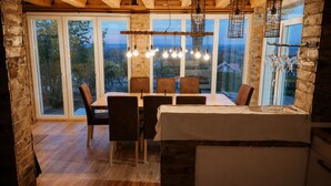 Een eethoek met een tafel en stoelen, grote ramen en hangende lampen.