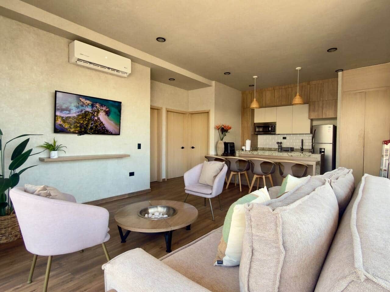 Ein modernes Wohnzimmer mit einer Couch, Sesseln, einem Couchtisch und einer Küchenzeile im Hintergrund.
