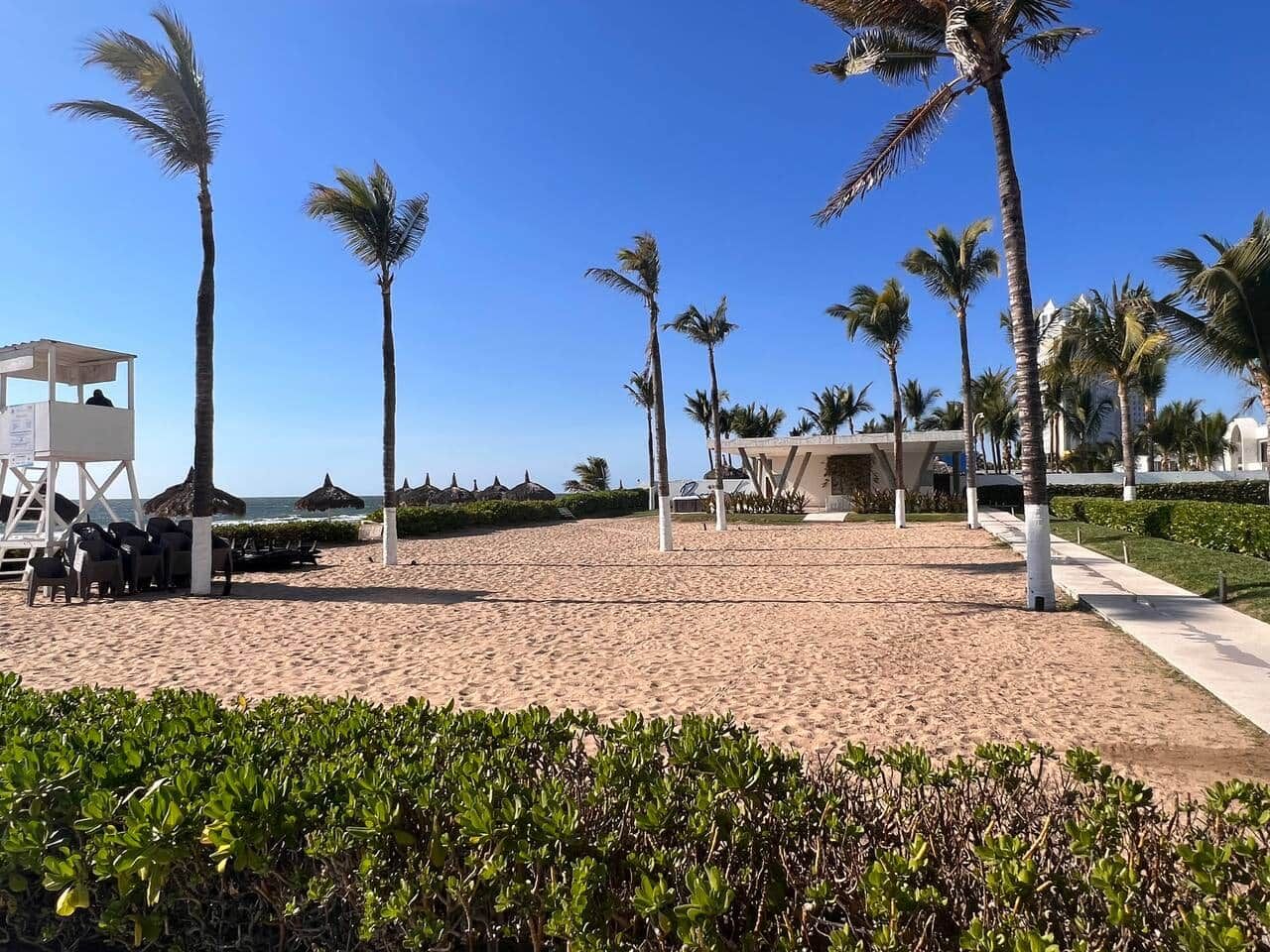 Une plage bordée de palmiers, une tour de surveillance pour les sauveteurs et un bâtiment au design moderne.