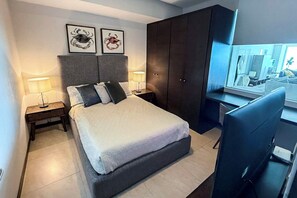 Un dormitorio moderno con una cama grande, dos lámparas de noche, un armario oscuro y un escritorio con una computadora.
