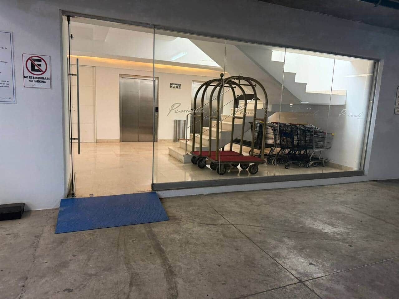 L’entrée d’un hôtel, avec une porte en verre, un panneau indiquant qu’il est interdit de se garer et un chariot à bagages à l’intérieur.