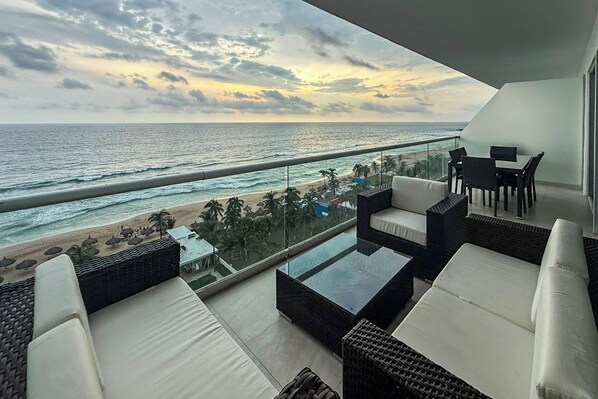Un balcon avec vue sur la plage et l’océan, aménagé avec des canapés en osier et une table basse en verre.