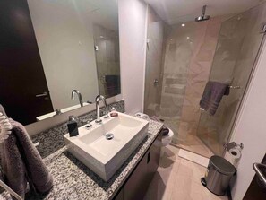 Une salle de bain moderne dotée d’un grand lavabo, d’une douche à parois de verre et d’un comptoir en marbre.