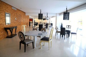 Ein großzügiger Essbereich mit modernem Design, ausgestattet mit einer Mischung aus Holz- und Polsterstühlen, einem Marmortisch und Pendelleuchten.