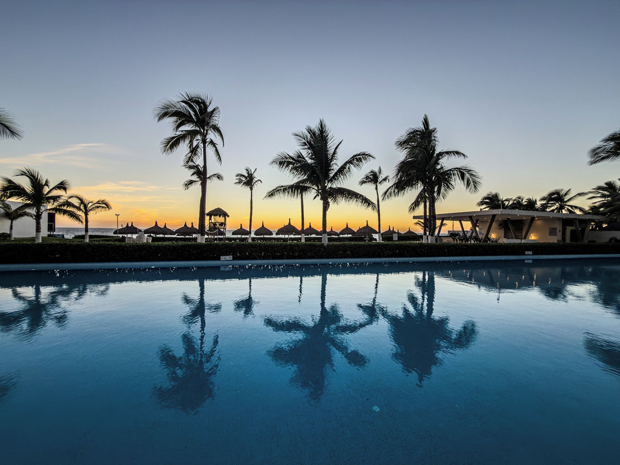 A pool reflecting palm trees and a resort building at sunset.