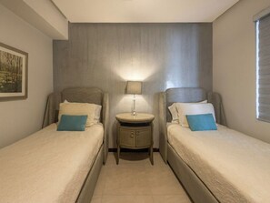 A twin room with two beds, a bedside table with a lamp, and a window.