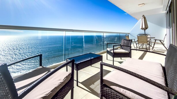 A balcony with a view of the ocean, wicker furniture, and a table. - Peninsula Mazatlan Floor 27: Exclusive 3-Bedroom Oceanfront (Mazatlan)