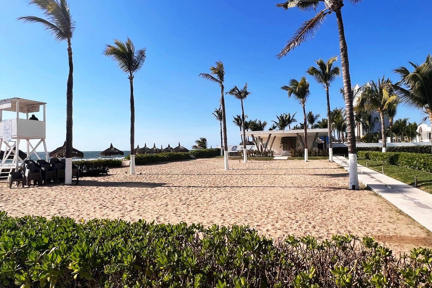 Ein Strand mit Palmen, einem Rettungsturm und einem Gebäude mit einem markanten Dach.