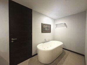 Un baño con una bañera blanca, una puerta, una obra de arte enmarco y un perchero para toallas.