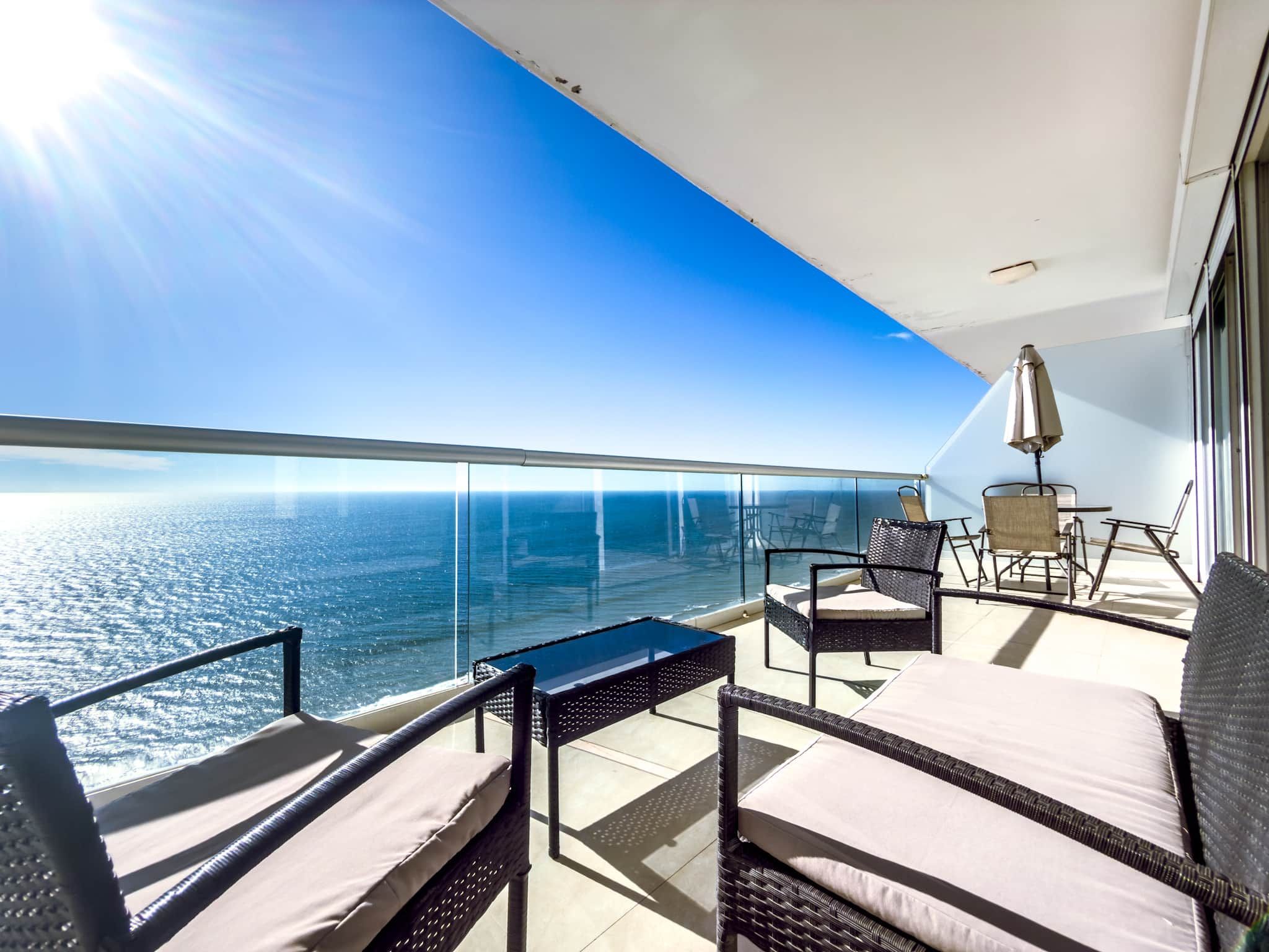 A balcony with a view of the ocean, wicker furniture, and a table.