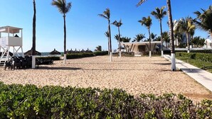 A beach with palm trees, a lifeguard tower, and a building with a unique roof design. - Peninsula Mazatlan Floor 27: Exclusive 3-Bedroom Oceanfront (Mazatlan)