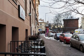 En gade med parkerede biler, udendørs siddepladser og bygninger med skilte.