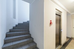 A staircase leading to an elevator in a hallway with white walls and a fire alarm on the wall. - Bosacka Downtown Apartment (Kraków)