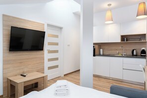 A modern hotel room with a flat-screen TV, a wooden headboard, a bedside table with a glass, and a neatly folded towel. - Bosacka Downtown Apartment (Kraków)