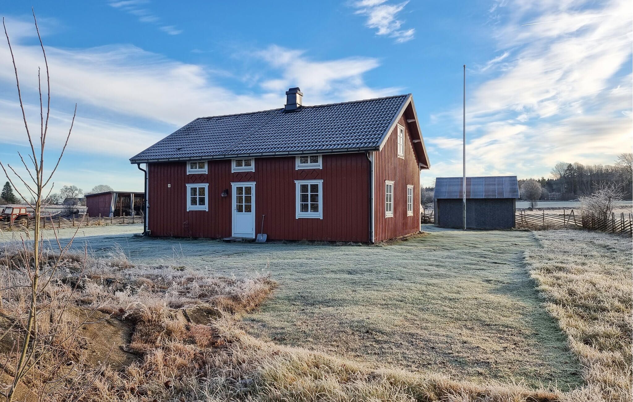 Une maison en bois rouge, avec un toit recouvert de tuiles, une porte blanche et deux fenêtres.
