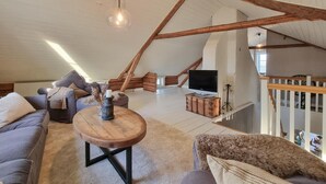 A spacious loft with a high ceiling, exposed wooden beams, a large window, a sofa, a coffee table, and a television. - Cozy home in Väby with WiFi (Väby)
