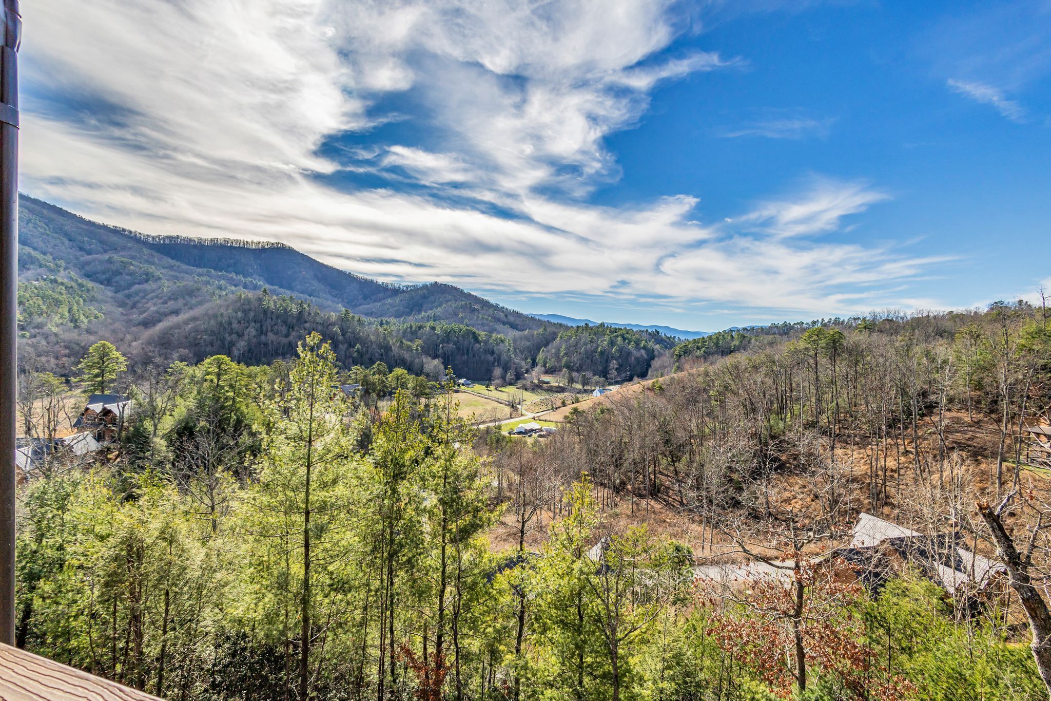 A mountainous landscape with a valley, dense forest, and a few buildings.