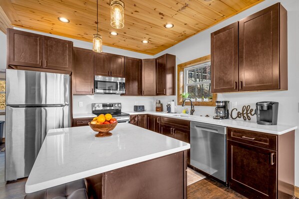 A modern kitchen with dark wood cabinets, stainless steel appliances, and a white island. - Epic Mountain Views-Wears Valley-Hot Tub-Dollywood-Family Fun! (Sevierville)