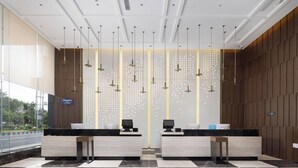 A hotel reception area with two reception desks, a check-in counter, and a decorative wall with hanging lights. - Hampton by Hilton Xiamen Tong'an Chengnan (Xiamen)