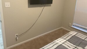 Un dormitorio con una cama, un televisor montado en la pared y una ventana con persianas.