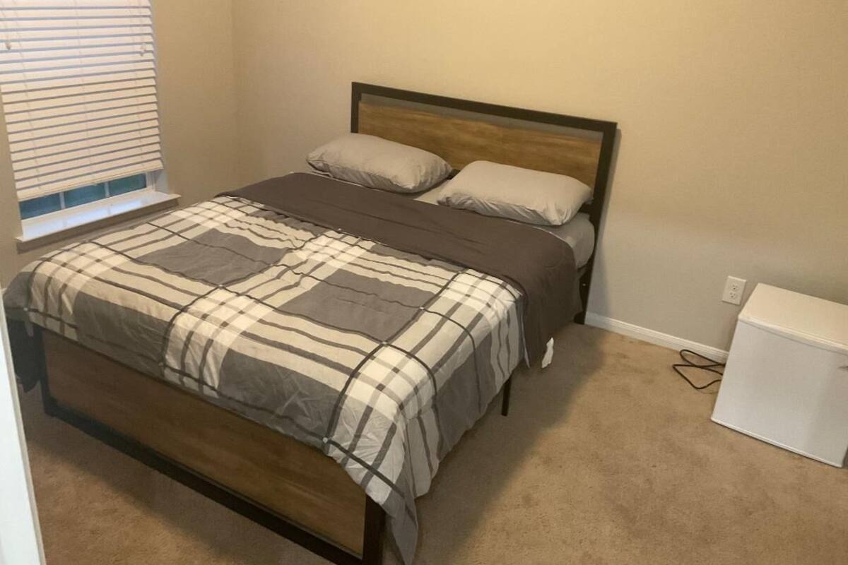 A bedroom with a wooden bed, a beige carpet, a window with blinds, and a white dresser.