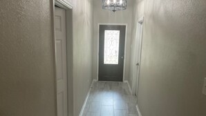 Un pasillo con piso de baldosas, una puerta al final e iluminación en el techo.